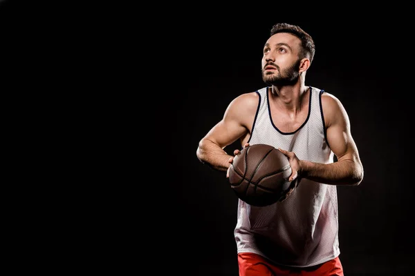 Handsome basketball player holding ball isolated on black — Stock Photo