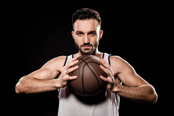 Jugador de baloncesto serio sosteniendo pelota aislado en negro - foto de stock