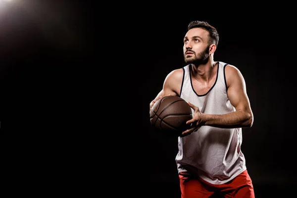 Ernsthafter Basketballspieler mit Ball auf schwarzem Hintergrund — Stockfoto