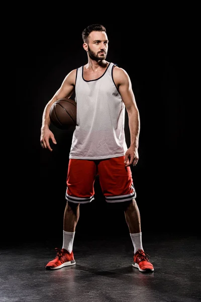 Muscular basketball player standing with ball on black background — Stock Photo