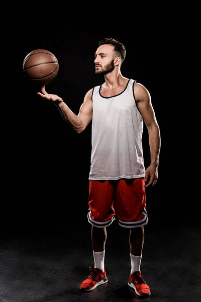 Schöner Basketballspieler, der Ball am Finger auf schwarzem Hintergrund dreht — Stockfoto