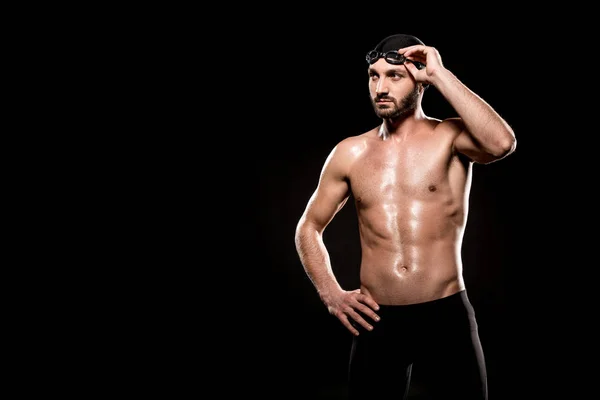 Nadador muscular em pé na touca de natação e tocando óculos de natação isolados em preto — Fotografia de Stock