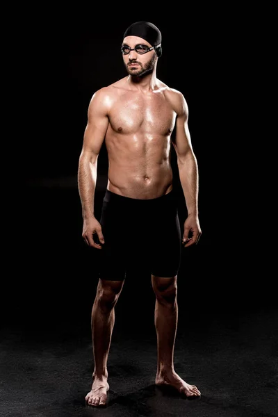 Confident swimmer standing in swimming cap and goggles on black background — Stock Photo