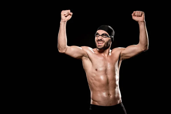 Cheerful swimmer standing in swimming cap and celebrating victory isolated on black — Stock Photo