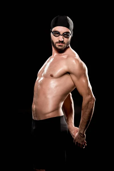 Muscular swimmer posing in swimming cap and goggles isolated on black — Stock Photo