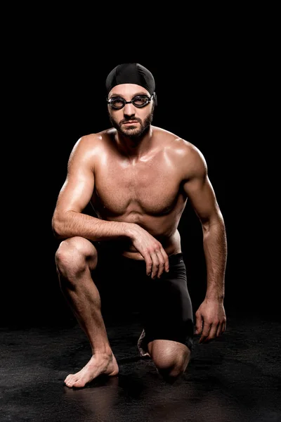Handsome swimmer sitting in swimming cap and goggles on black background — Stock Photo