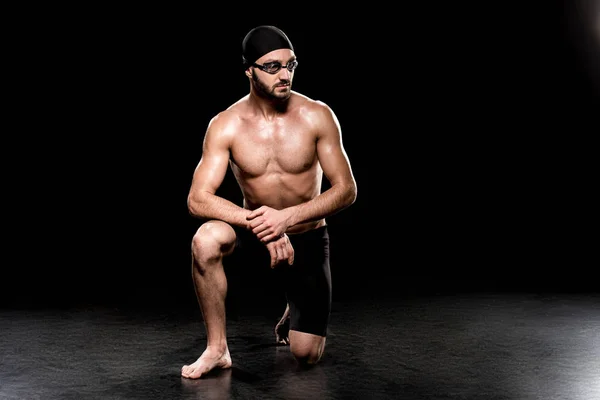 Athletic man sitting in swimming cap and goggles on black background — Stock Photo