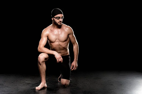 Athletic sportsman sitting in swimming cap and goggles on black background — Stock Photo
