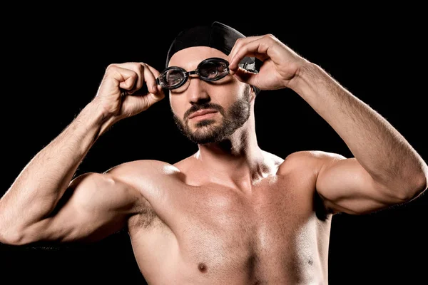 Атлетический спортсмен, стоящий в плавательной шапке и касающихся очков, изолированных на черном — стоковое фото