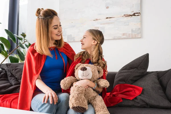 Fröhliche Mutter und Kind in roten Mänteln halten Teddybär in der Hand und schauen einander an — Stockfoto