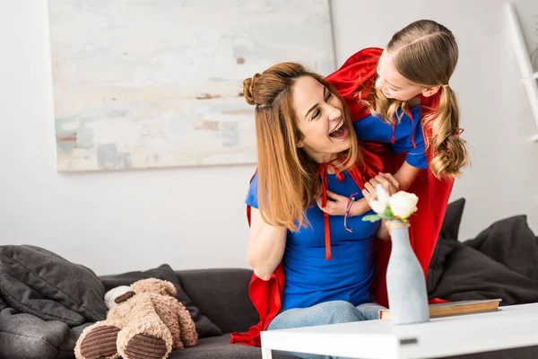 Smiling mother and daughter in red cloaks hugging and looking at each other — Stock Photo