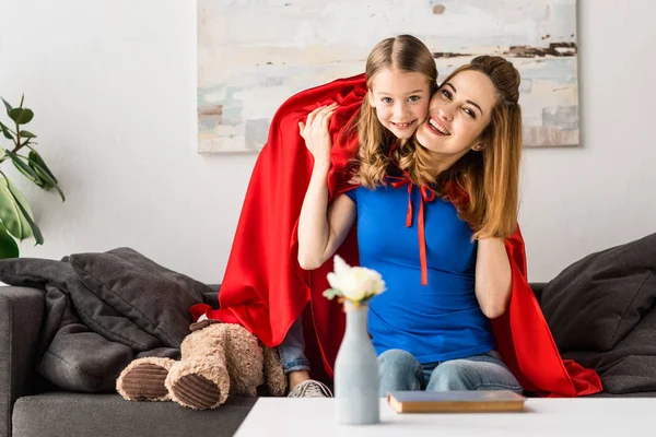 Smiling mother and cute kid in red cloaks looking at camera — Stock Photo