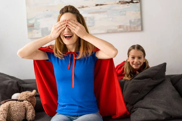 Mother and kid in red cloaks playing hide-and-seek at home — Stock Photo