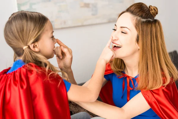 Hermosa madre y linda hija en capas rojas jugando en casa - foto de stock