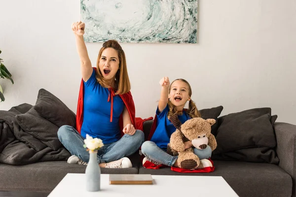 Emocionados madre e hija sentadas en el sofá y riendo en casa - foto de stock