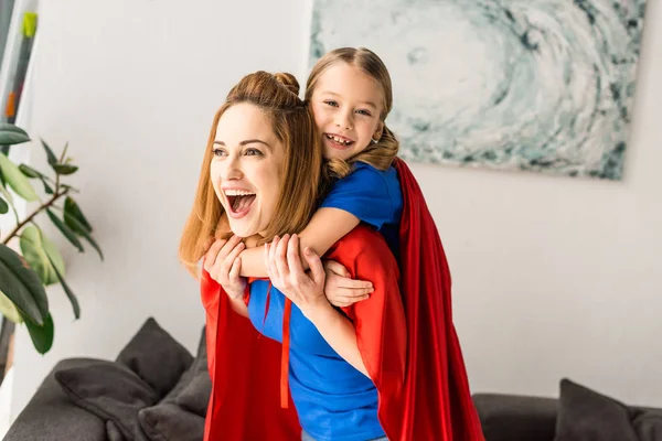 Mãe e filha alegres em capas vermelhas brincando em casa — Fotografia de Stock