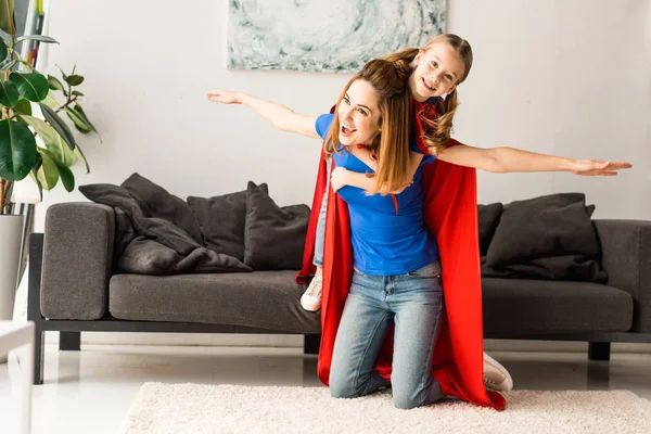 Cute kid and mother in red cloaks playing at home — Stock Photo