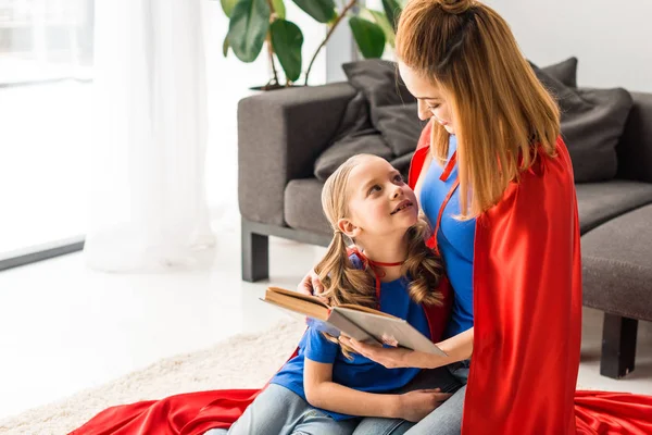 Daughter and mother in red cloaks holding book and looking at each other — Stock Photo