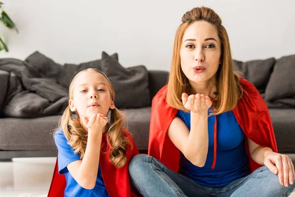 Hija y madre en capas rojas soplando besos de aire - foto de stock