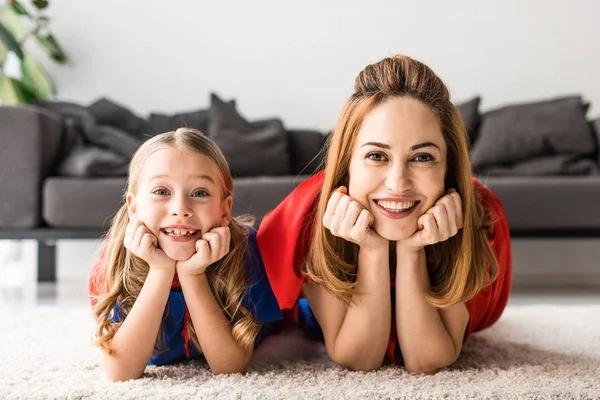 Smiling daughter and mother looking at camera on floor — Stock Photo