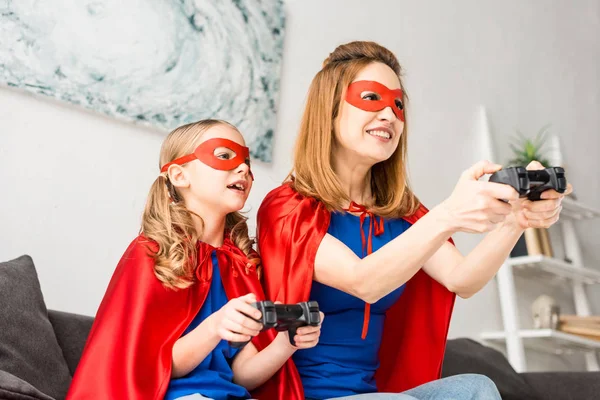 Mother and daughter in red masks and cloaks playing video game — Stock Photo