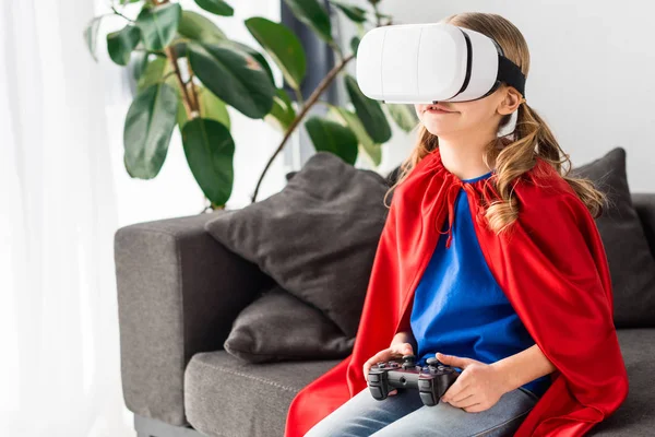 Lindo niño en capa roja y auriculares de realidad virtual jugando videojuego - foto de stock