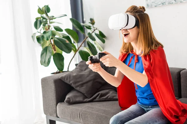 Усміхнена мати в червоному плащі та гарнітура віртуальної реальності грає у відеоігри — стокове фото