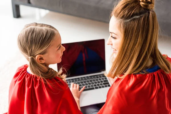 Back view of mother and daughter in red cloaks holding laptop — Stock Photo