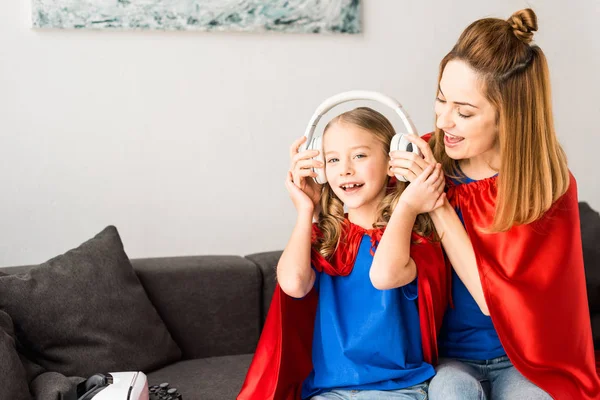 Cute kid and beautiful mother in red cloaks holding headphones — Stock Photo