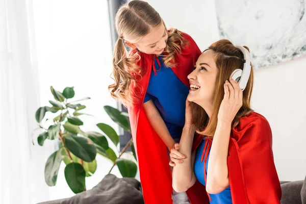 Mãe atraente em fones de ouvido brancos e filha sorridente olhando um para o outro — Fotografia de Stock