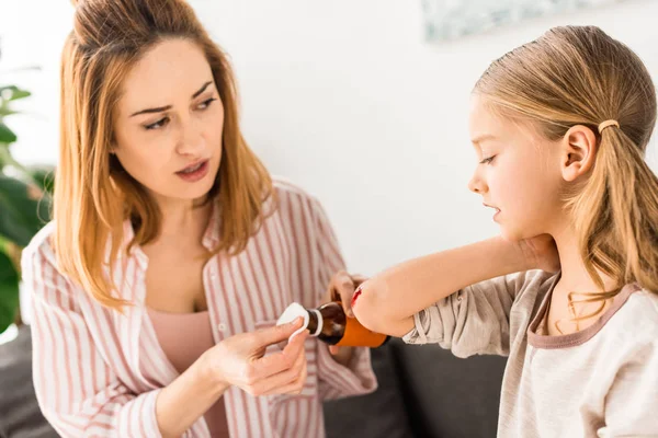 Attractive mother treating injured kid with antiseptic at home — Stock Photo