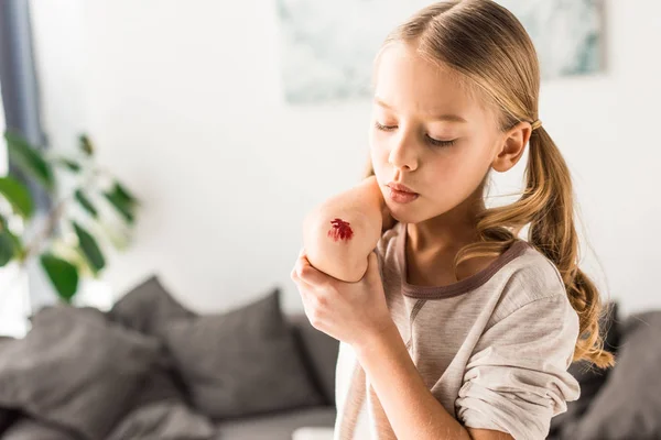 Sad kid blowing on wound at home — Stock Photo