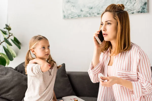 Upset mother talking on smartphone and daughter with wound sitting on table — Stock Photo