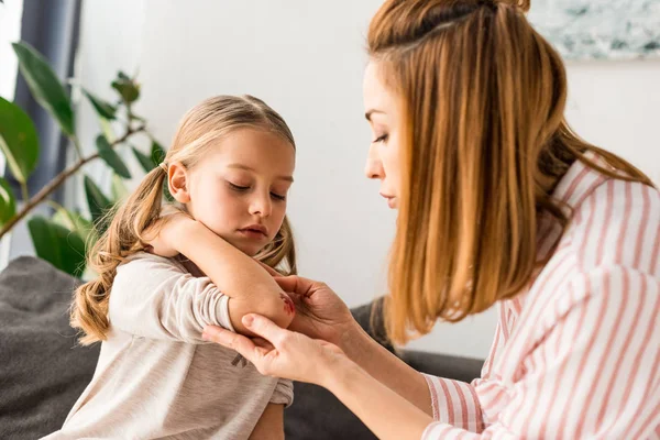 Atractiva madre cuidando hija lesionada en casa - foto de stock