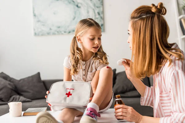 Schöne Mutter behandelt verletzte Tochter zu Hause mit Antiseptikum — Stockfoto