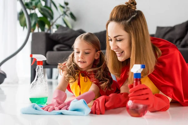 Mãe e criança em capas vermelhas e luvas de borracha com sprays piso de lavagem — Fotografia de Stock