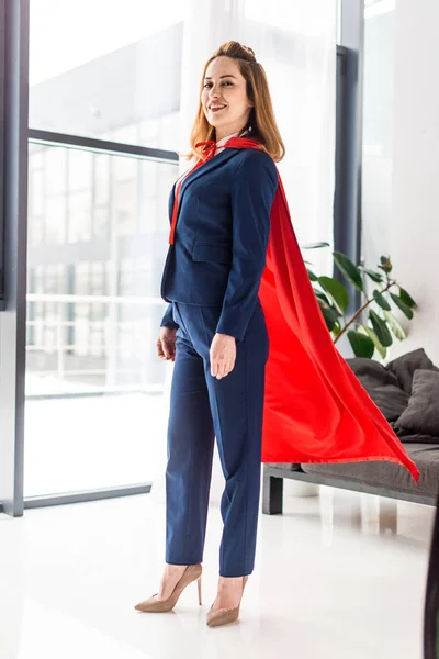 Femme d'affaires en costume bleu et cape rouge regardant la caméra — Photo de stock