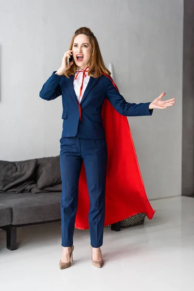 Screaming businesswoman in blue suit and red cape talking on smartphone — Stock Photo