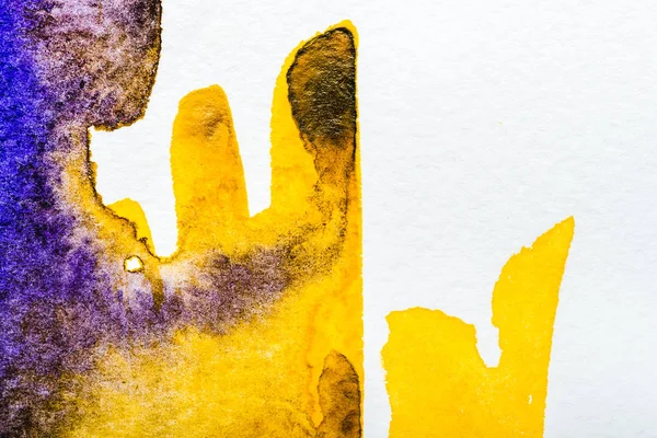 Vista superior de los derrames de acuarela amarilla y púrpura sobre papel blanco - foto de stock