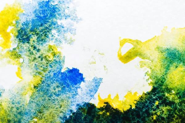 Vue de dessus des déversements d'aquarelle bleue et jaune sur papier blanc — Photo de stock