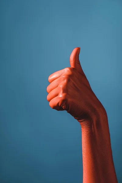 Vista recortada de la mujer que muestra el pulgar hacia arriba en la mano de color coral sobre fondo azul, el color del concepto 2019 - foto de stock