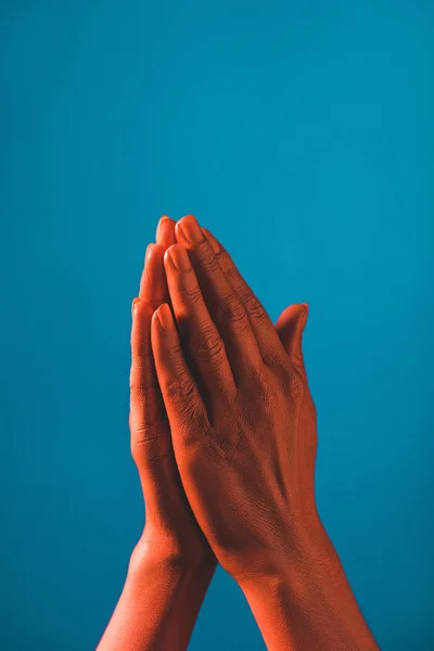Частичный вид женщины, показывающей знак молитвы коралловым цветом рук на синем фоне, цвет концепции 2019 года — стоковое фото