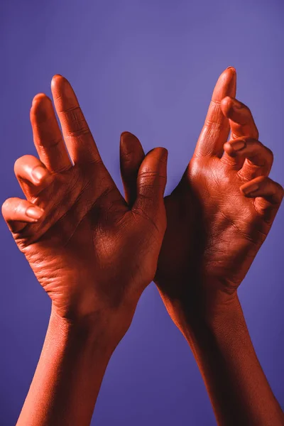 Partial view of woman showing bird sign by coral colored hands on violet background, color of 2019 concept — Stock Photo