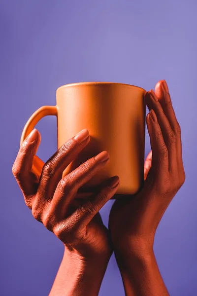 Частковий вигляд жінки з кораловими кольоровими руками, що тримає чашку кольорової кави на фіолетовому фоні, колір концепції 2019 року — Stock Photo