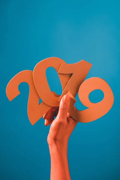 Vue partielle des mains féminines de couleur corail avec du papier découpé numéros 2019 sur fond bleu, couleur du concept 2019 — Photo de stock