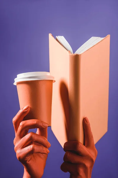 Vista parcial de las manos femeninas de color coral con taza de papel de coral y libro sobre fondo azul, concepto de color de 2019 - foto de stock