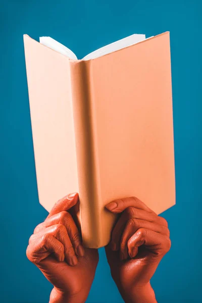 Vista recortada de la mujer con las manos de color coral sosteniendo libro de coral sobre fondo azul, color de 2019 concepto - foto de stock