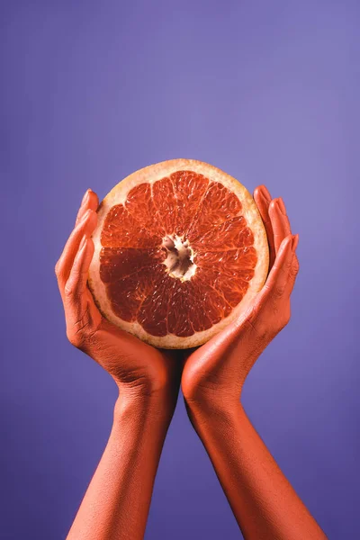 Vista parcial de la mujer sosteniendo toronja cortada en manos de color coral sobre fondo azul, concepto de color de 2019 — Stock Photo
