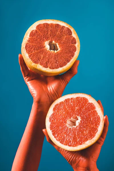 Обрізаний вид жінки, що тримає половинки грейпфрута в коралових кольорових руках на синьому фоні, колір концепції 2019 року — стокове фото