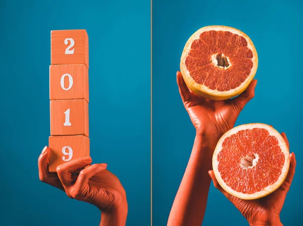 Collage con cubos de madera con números 2019 y mitades de pomelo en manos femeninas de color coral sobre fondo azul separado, concepto de color de 2019 - foto de stock